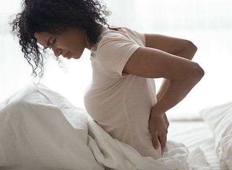 Woman sitting in bed with back pain, possibly suffering from fibromyalgia